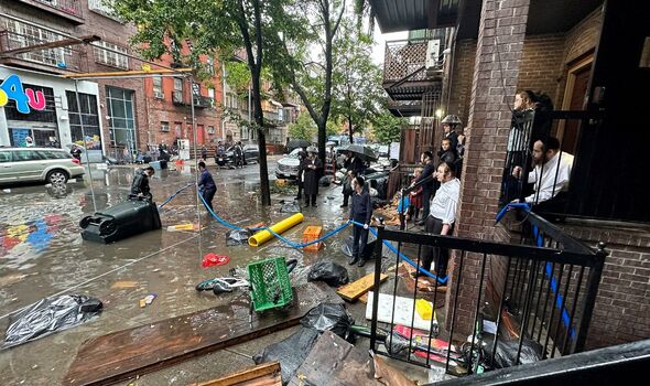 People look on as debris-filled floodwaters lap at their front porch.